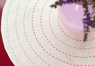 Anna Maria Horner puts her contemporary take on the traditional doily. She shows you how to create a reversible doily with concentric rings of running stitches in a beautiful spectrum.