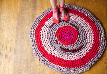 Two feet standing on a multicolored crocheted rag rug resting on a wood floor
