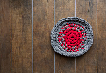 A small crocheted circle made out of torn fabric pieces, sitting on a wooden floor.