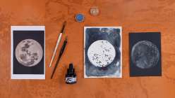 An overhead image of a monoprinted image of the moon made with acrylic ink and watercolor.
