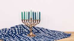 A menorah with handmade beeswax candles in various shades of blue set on an indigo tablecloth.
