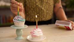 A hand lighting a cupcake on a pedestal with a small dish holding a cupcake next to it.