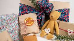 A pile of colorful packages plus a small light brown stuffed teddy bear.