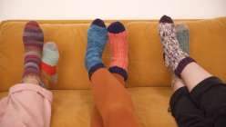 the pairs of colorful handmade socks on three pairs of feet on the couch 