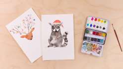 Two images of whimsical animals in holiday attire, including a reindeer with ornaments hanging from its antlers and a raccoon with a Santa hat eating a candy cone, both from Maria Carluccio's Celebrate the Season Daily Holiday Painting Practice class on C