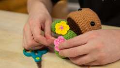 A pair of hands attaching a flower to a crocheted flowerpot from Vincent Green-Hite's Amigurumi Techniques: Finish Off a 3D Project class
