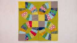 A completed block from Sarah Bond's Creativebug Pickle Dish Quilt Block class in shades of chartreuse, yellow, grey, blues and reds