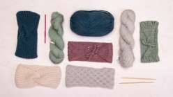 Overhead shot of a table laid with four knit headbands, two skeins of yarn, and a pair of knitting needles from Faith Hale's Creativebug Knit Headbands: Three Ways class
