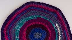 A crocheted rag rug in shades of turquoise, pink, purples and blues