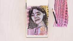 An overhead image of a portrait of a woman drawn in purple on an open book, taken from Creativebug's Altered Books Daily Practice class