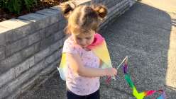 A toddler wearing a rainbow silk play cape from the Easy Dyed Silk Play Cape class by Melissa Lang Lytle on Creativebug