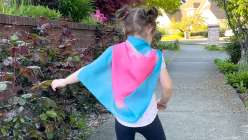 A toddler wearing a blue and pink silk play cape from the Easy Dyed Silk Play Cape class by Melissa Lang Lytle on Creativebug
