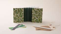 An accordion book with a green spine and green decorative papers made by e bond in her Accordion Book as Art Form class on Creativebug