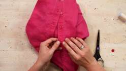 Two hands sewing a pink button onto a pink shirt from Faith Hale's How to Sew On a Button technique class on Creativebug