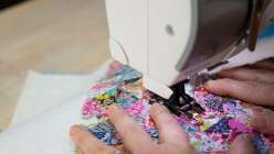 The image of hands pushing a patchwork piece of fabric through a sewing machine from Blair Stocker's Sew a Stash-Busting Stocking class on Creativebug