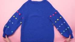 A cobalt blue sweater with colorful bobbles on the sleeves made in Twinkie Chan's Design and Crochet a Top-Down Bobble Sweater class on Creativebug.