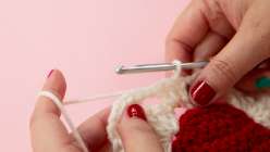 Twinkie Chan crocheting a granny square using white and red yarn in her Crochet a Strawberry Granny Square class on Creativebug