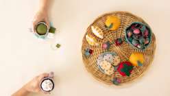 A rattan platter of felt food including strawberries, oranges, and cookies, surrounded with two mugs of tea, all made in Sanae Ishida's Sew Felt Play Food class on Creativebug.