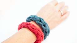 A hand wearing a red finger knit necklace and turquoise finger knit bracelet made in Faith Hale's Finger Knitting class on Creativebug.