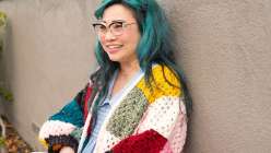 Twinkie Chan wearing a multicolored crochet sweater with yellow ribbed cuffs that she made in her Crochet a Granny Square Cardigan class on Creativebug. 