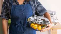 A person wearing an apron holding a bowl partially covered with a fabric bowl cover made in the Creativebug class Sew Reusable Bowl Covers.