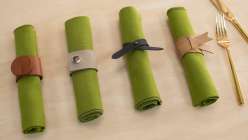 Four green napkins with a four styles of leather napkin rings made in the Make Leather Napkin Rings class on Creativebug