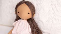 A hand-sewn doll with tan skin and brown hair, wearing a light pink, all made in Katia Ferris's Sew a 14-Inch Rag Doll class on Creativebug.