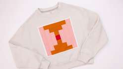 A cream colored sweatshirt with an ochre and pink quilt block stitched to the front, made in Faith Hale's Make a Quilt Block Sweatshirt class on Creativebug.