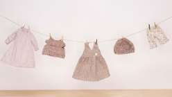 A miniature clothesline holding a dress, a sweater, a pinafore, a knit hat, and a pair of shorts, made by Katia Ferris in her Sew a Wardrobe for a 14-Inch Rag Doll class on Creativebug.